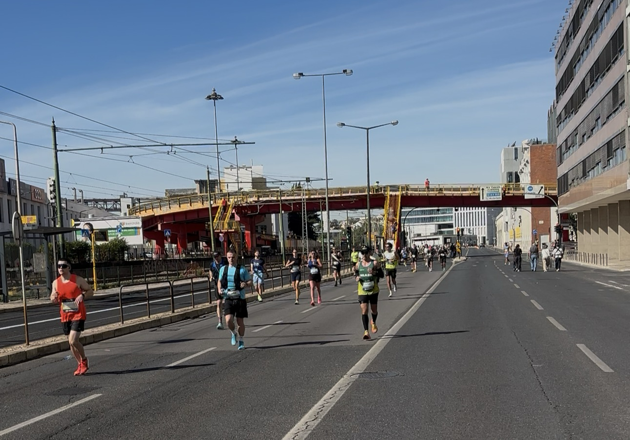 Coureurs sur une avenue de Lisbonne pendant le marathon, sous un ciel bleu.